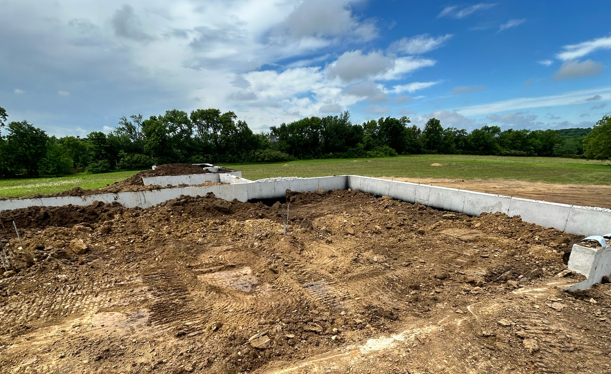 Concrete foundation in dirt field, green trees behind.