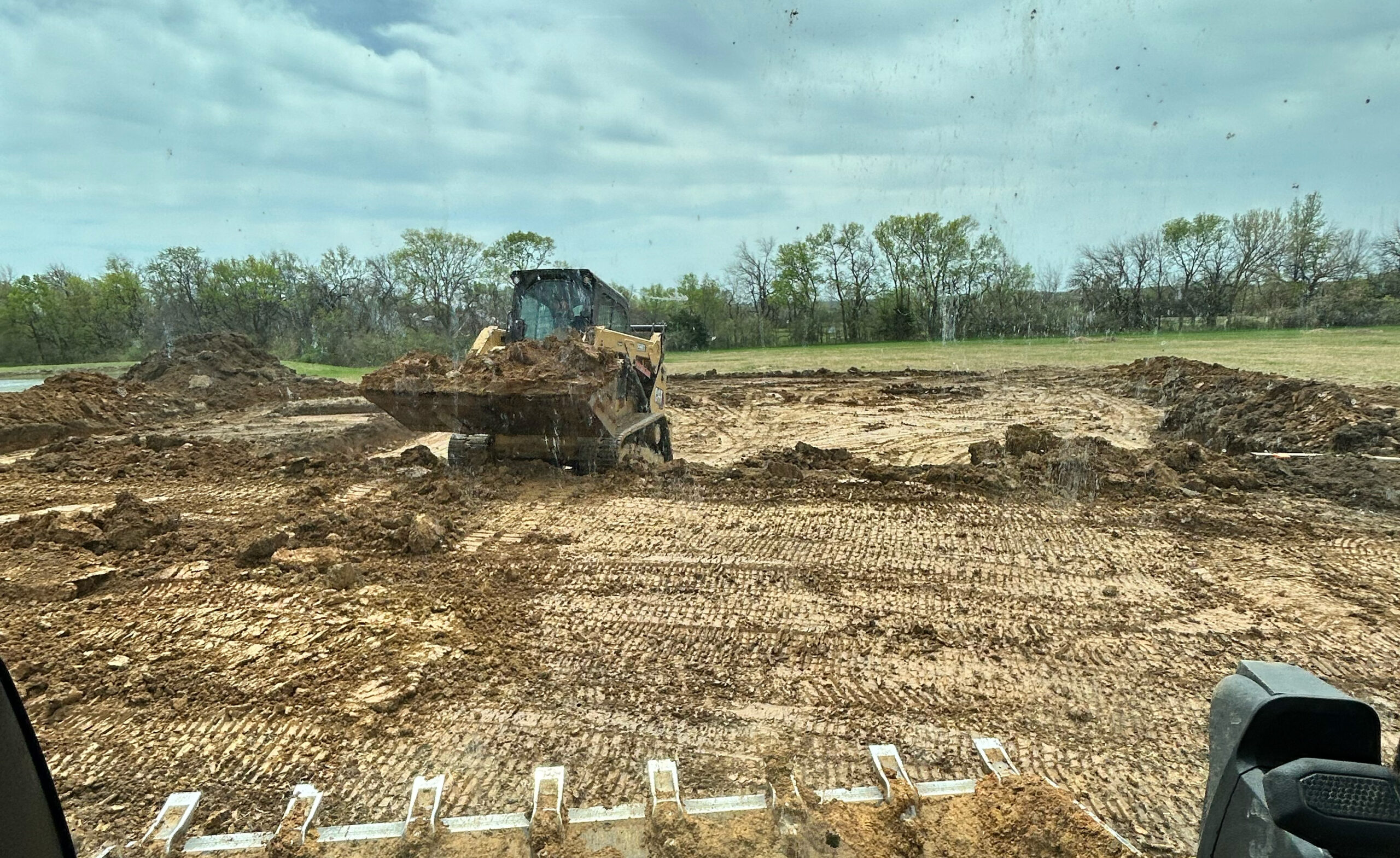 Skid steer moving wet, muddy dirt in a construction field.