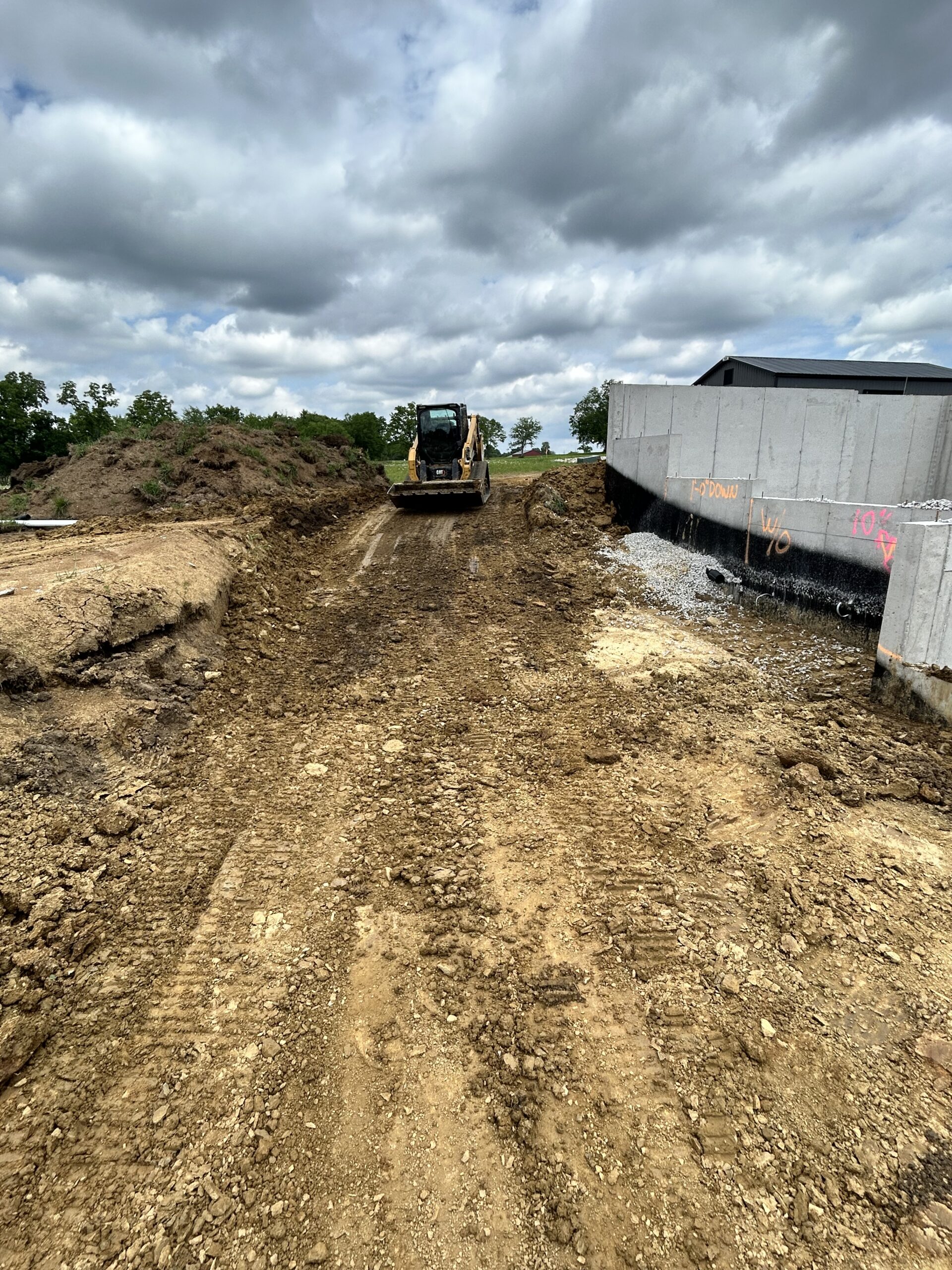 Skid steer approaching concrete retaining wall on muddy site.