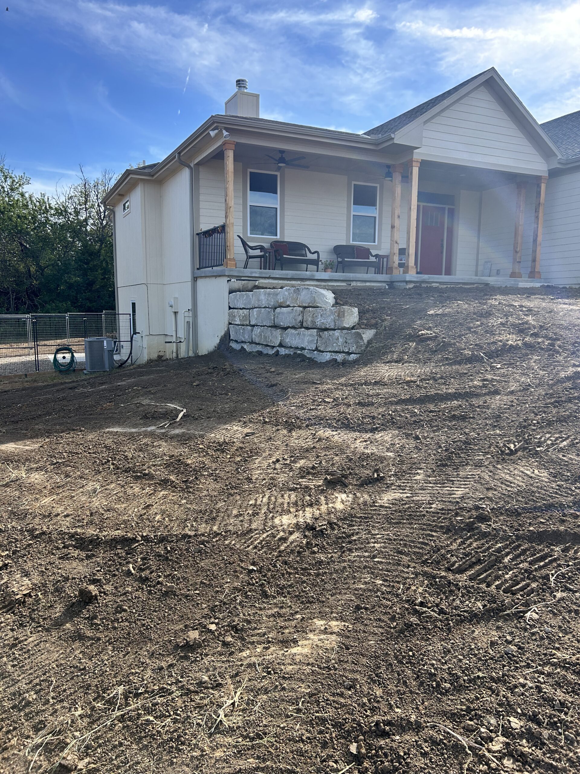 Dirt yard sloping up to house with patio and stone retaining wall.