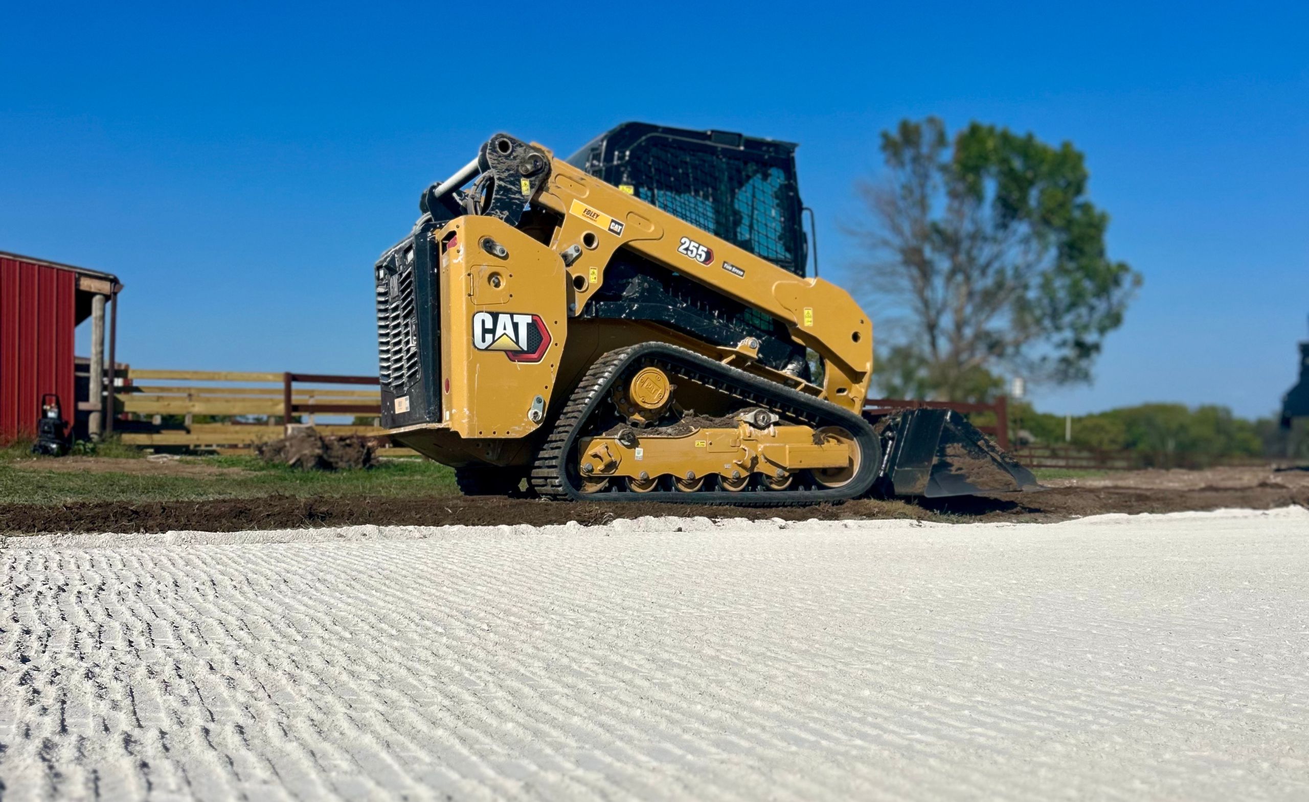 CAT 255 skid steer on white stone foundation, red barn.