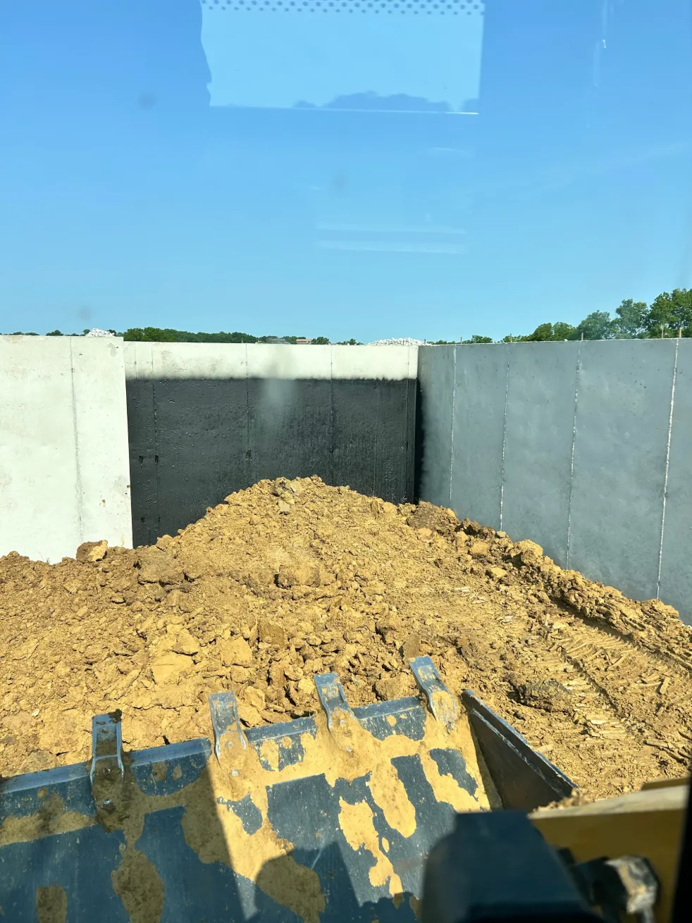View from skid steer bucket toward black and white concrete wall.